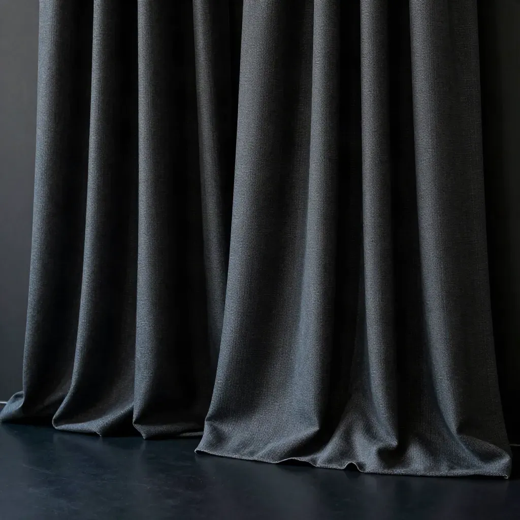 Tende oscuranti carbone in studio scuro, pieghe pesanti e luce blu radente.
